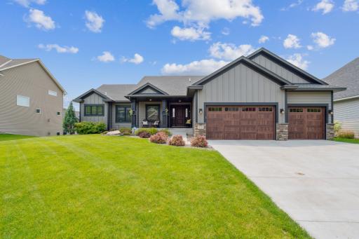 Stunning modern craftsman home with eye-catching curb appeal, featuring rich wood garage doors, stone accents, a welcoming front porch, and a beautifully landscaped lawn.