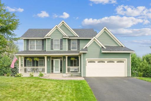 Beautiful curb appeal with updated green siding, charming front porch, and an American flag waving proudly. Spacious driveway leads to a two-car garage.