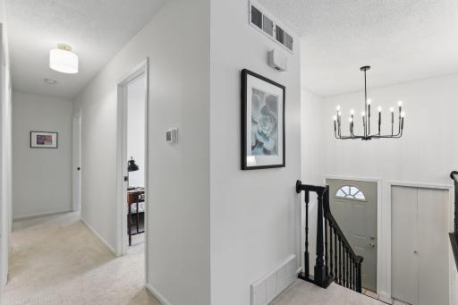 Hallway leading to all three bedrooms, featuring fresh carpet, white trim, and updated doors for a clean, cohesive look.