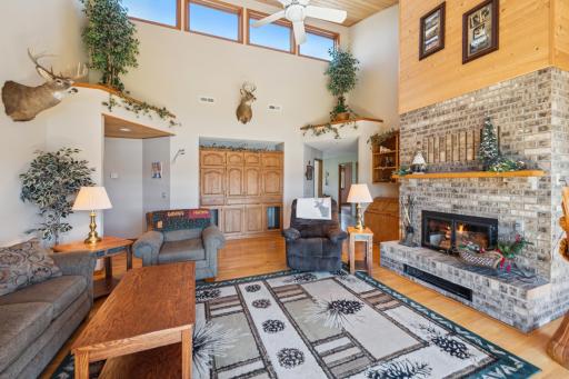 Spacious vaulted living room with brick fireplace, built-ins, and large upper windows allowing natural light to fill the space.