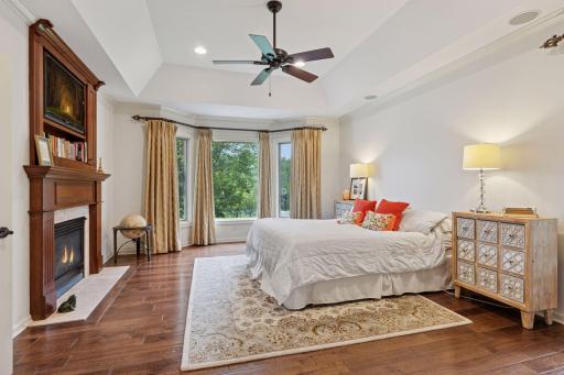 The main floor primary bedroom suite offers hardwood floors, a tray vaulted ceiling, gas fireplace and views of the lake.
