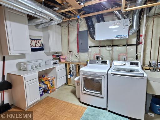 The large capacity washer and electric dryer were brand new in 2024 and sit among the mechanicals for a clean space. The white cabinets offer additional storage and room for folding.