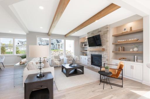 The great room is finished with rich wooden beams and the gas fireplace with stone surround is flanked by display shelves.