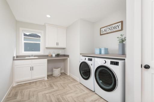The very bright and clean laundry room with a sink, storage cabinets and folding counter.