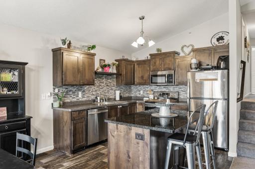 Dark cabinetry, granite island countertop, and a tile backsplash add an elevated feel to this kitchen.