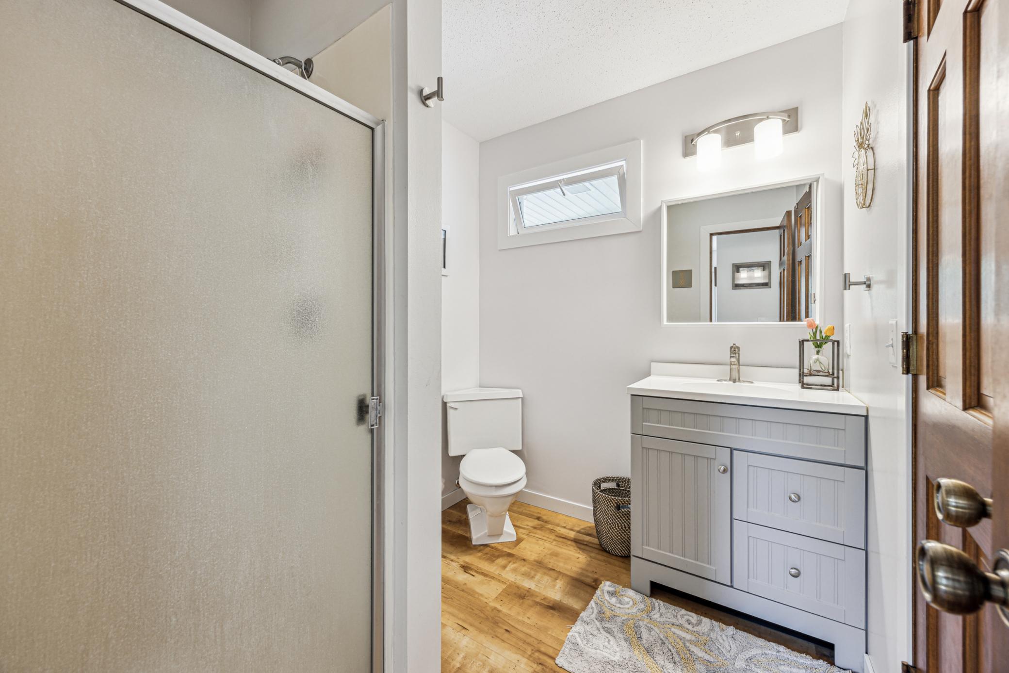 The tastefully updated main-level bathroom is tucked away for privacy and features a modern shower, stylish vanity, bright lighting and a large mirror, making this bathroom perfect for starting your day.
