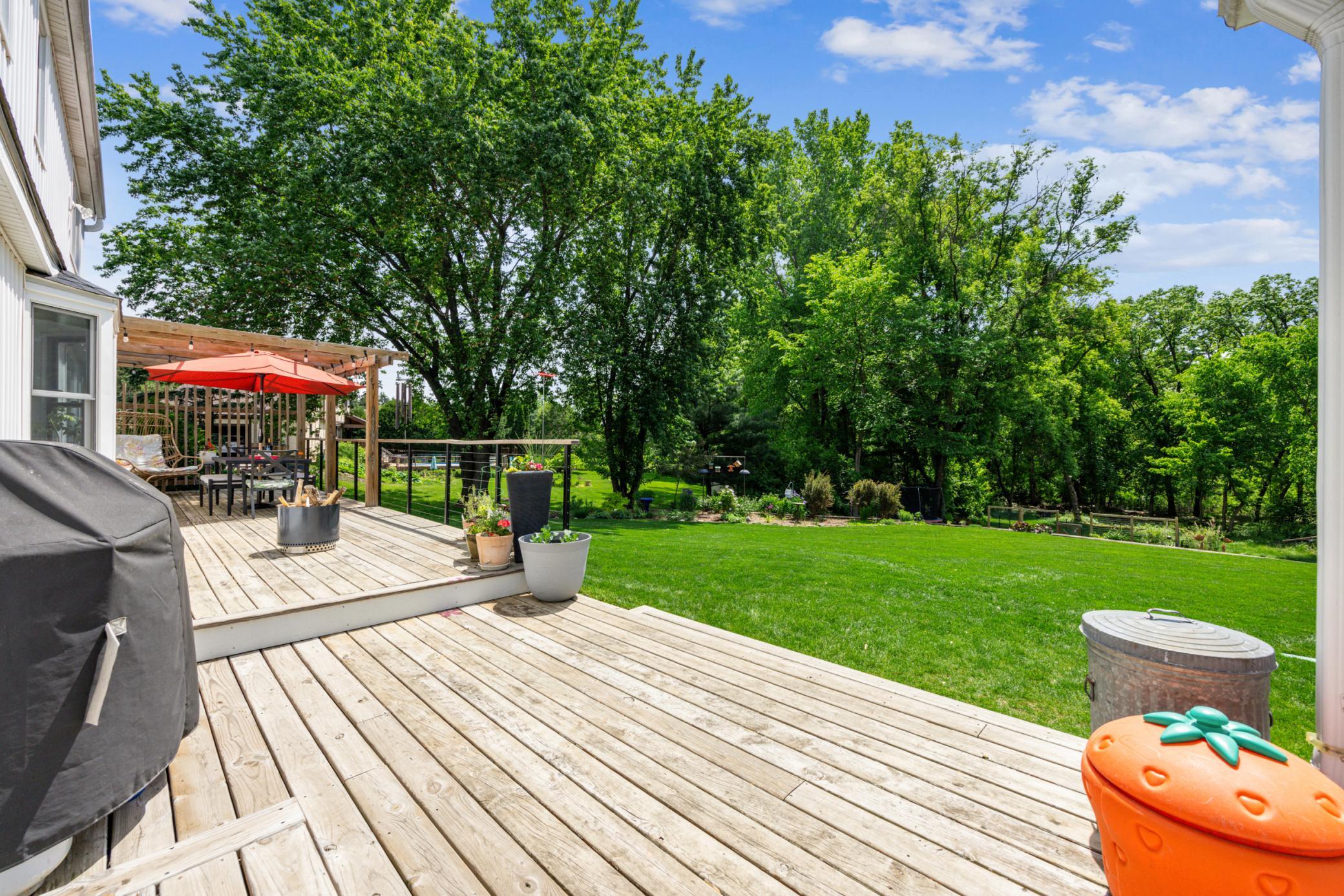 Stepping out onto the expansive deck overlooking a golf course-style yard and vibrant flower gardens, you can see this space is designed for comfort and entertainment. Beyond, a bonfire pit and mature trees create a tranquil retreat.