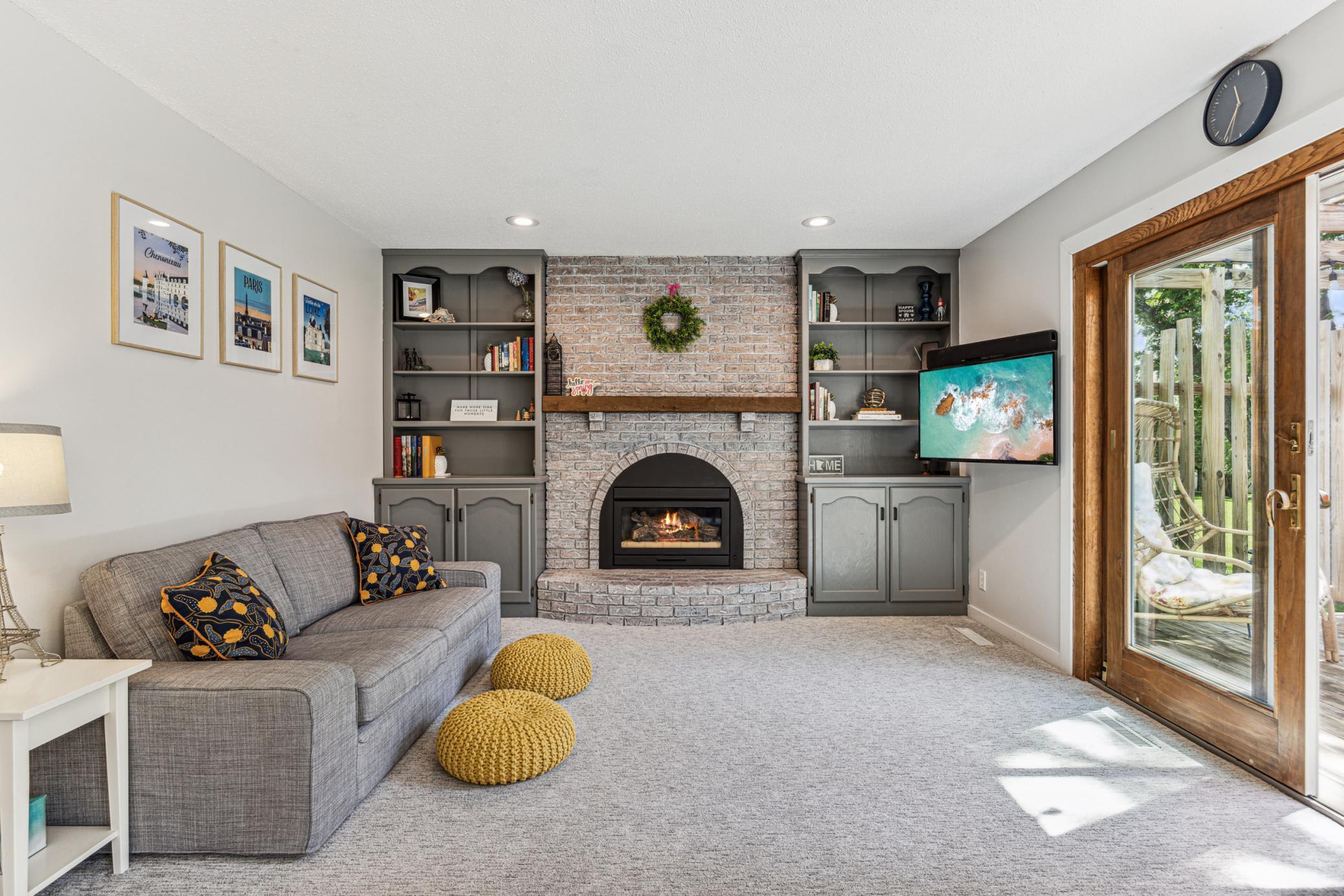 The living room showcases a gas fireplace with a classic brick surround, built-in bookshelves, and a patio door that opens to the deck.