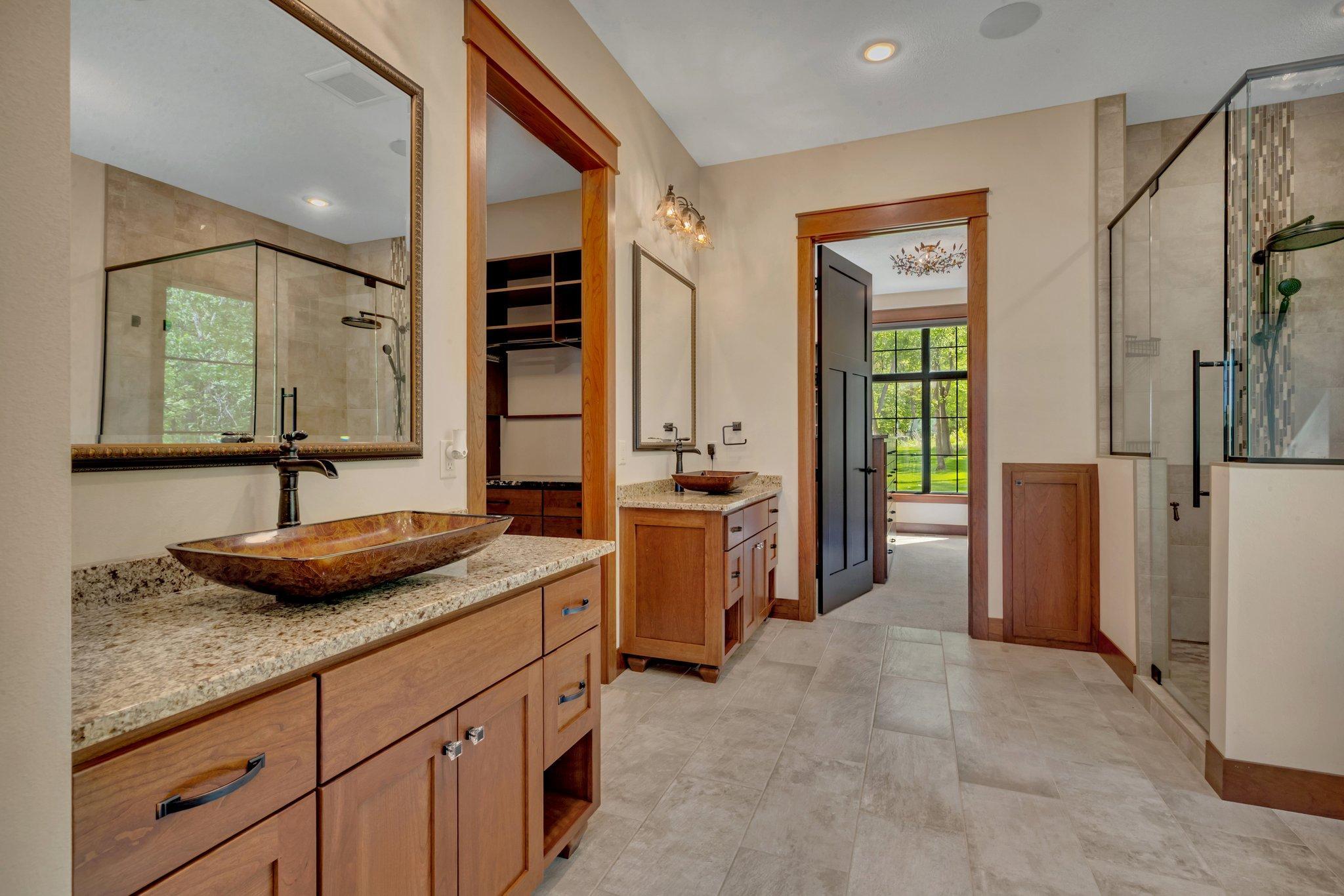 Modern glass-enclosed shower features a rainfall showerhead and mosaic tile accents. Parallel the shower sits a deep soaking tub, perfect for relaxing.