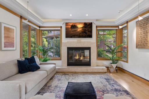 This Sitting Room/formal living room features windows on all sides, a gas fireplace with natural stone surround, accent pendant lighting, built-in art display cabinetry, and an included TV.