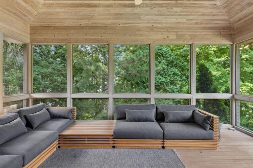 The covered outdoor lounge features wooded views, and walks out to the main level deck which overlooks the rear yard and pool.