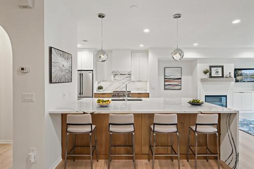 $260k Ispiri High-end Professional Remodel! This kitchen showcases a sleek, modern design with a striking waterfall island, minimalist cabinetry, and white oak wood flooring, all unified by elegant marble veining and contemporary lighting.
