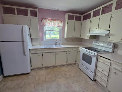 Bright kitchen has solid surface countertops, newer stove and refrigerator.