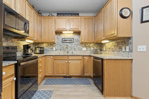 Updated Kitchen with solid surface countertops, black stainless steel appliances, tiled backsplash, under cabinet lights, and laminate floors