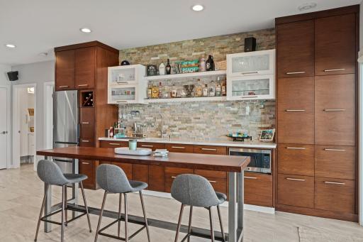 The bar features a fully equipped kitchenette complete with a refrigerator, sink, microwave, wine rack, and hanging glass storage