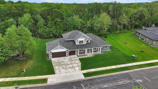 A wider aerial view showcases the home's manicured lawn, oversized driveway, and serene wooded backdrop. The lot is perfectly situated to provide privacy and curb appeal in a sought-after neighborhood.
