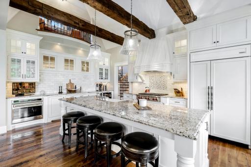 Custom enameled cabinetry with lighted glass displays, crown molding tops, decorative wainscoted hood above the gas cooktop, a multitude of both cabinets & drawers, and under cabinet lighting.