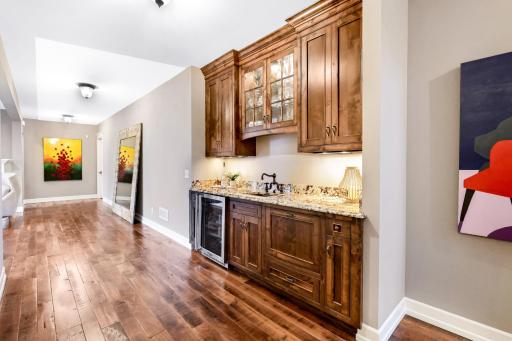 Handsome adjoining bar area with natural wood cabinetry, granite counters, sink, beverage fridge and pull-out dishwasher drawer with integrated panel front.