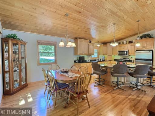 The dining area is framed by natural light and gleaming hardwood floors, all set beneath a warm wood-paneled vaulted ceiling that adds charm.