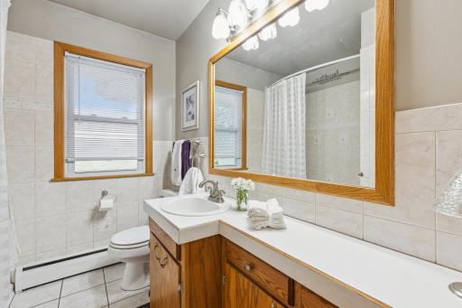 Main level full bathroom with storage cupboards, tiled floors and shower