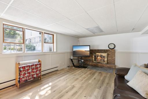 Lower-level large family room is remodeled with new vinyl plank flooring, board and batten wainscoting, and warm white paint. The family room has a wood burning fireplace perfect for our cozy fall and winter days.