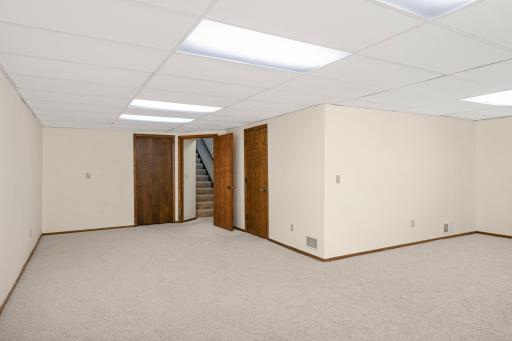 View of the lower-level rec room facing the stairs. The door on the right leads to the mechanical/workshop room, while the door to the left of the stairs opens to the laundry area.
