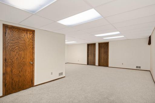 Spacious lower-level family and rec room with space for gaming. Left door leads to mechanical/workshop; two doors at the far end open to bonus rooms—ideal for offices, fitness, hobby or future bedrooms with added egress windows.