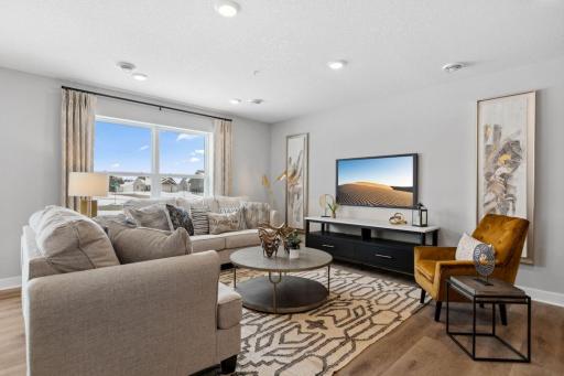 Welcome Home to The Harlow! The spacious living room flows seamlessly to the dining and kitchen. Photo of a similar layout model home, layout and colors will vary.