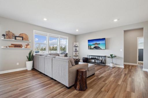 Large triple windows frame scenic views of the lush backyard, filling the room with natural light, while recessed lighting adds a warm, inviting ambiance.