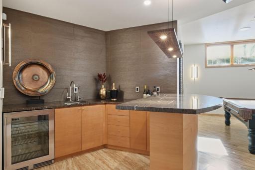The bar area boasts sleek granite countertops, a wine fridge, and stylish horizontal wall tiling
