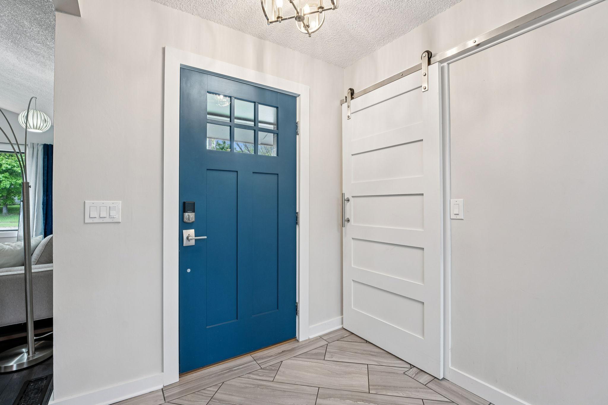 Stylish foyer featuring a statement blue front door, modern tile flooring, and a sleek white barn door. A fresh, bright first impression!