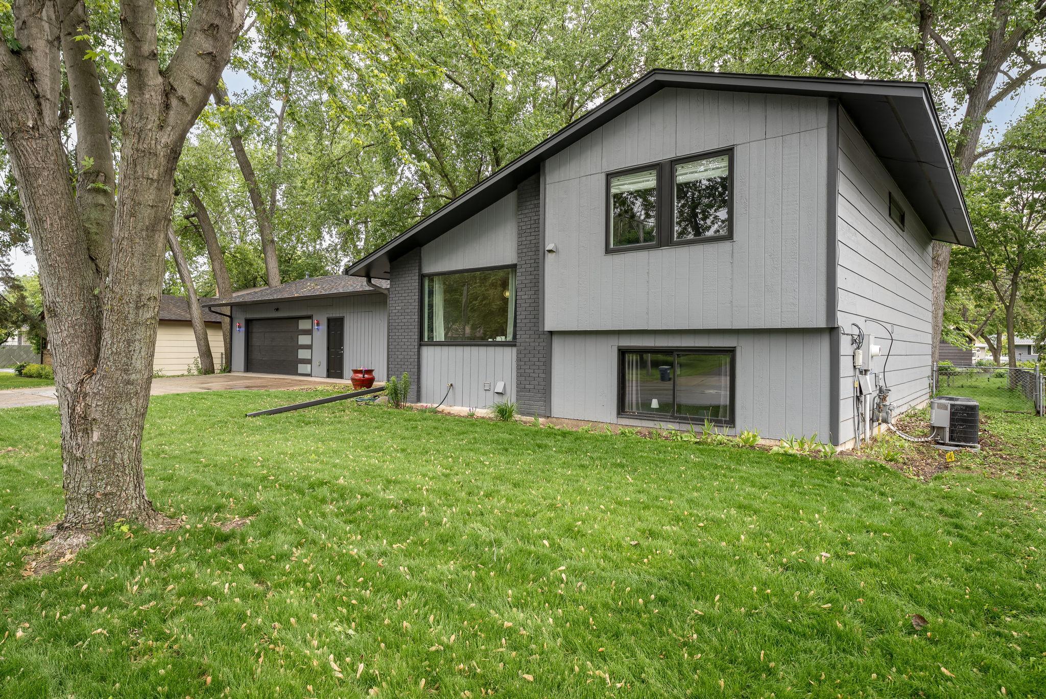 Side angle view showcasing the home's clean architectural, and large front windows that let in abundant natural light. Set on a generous lot with a lush, green lawn and mature tree coverage.