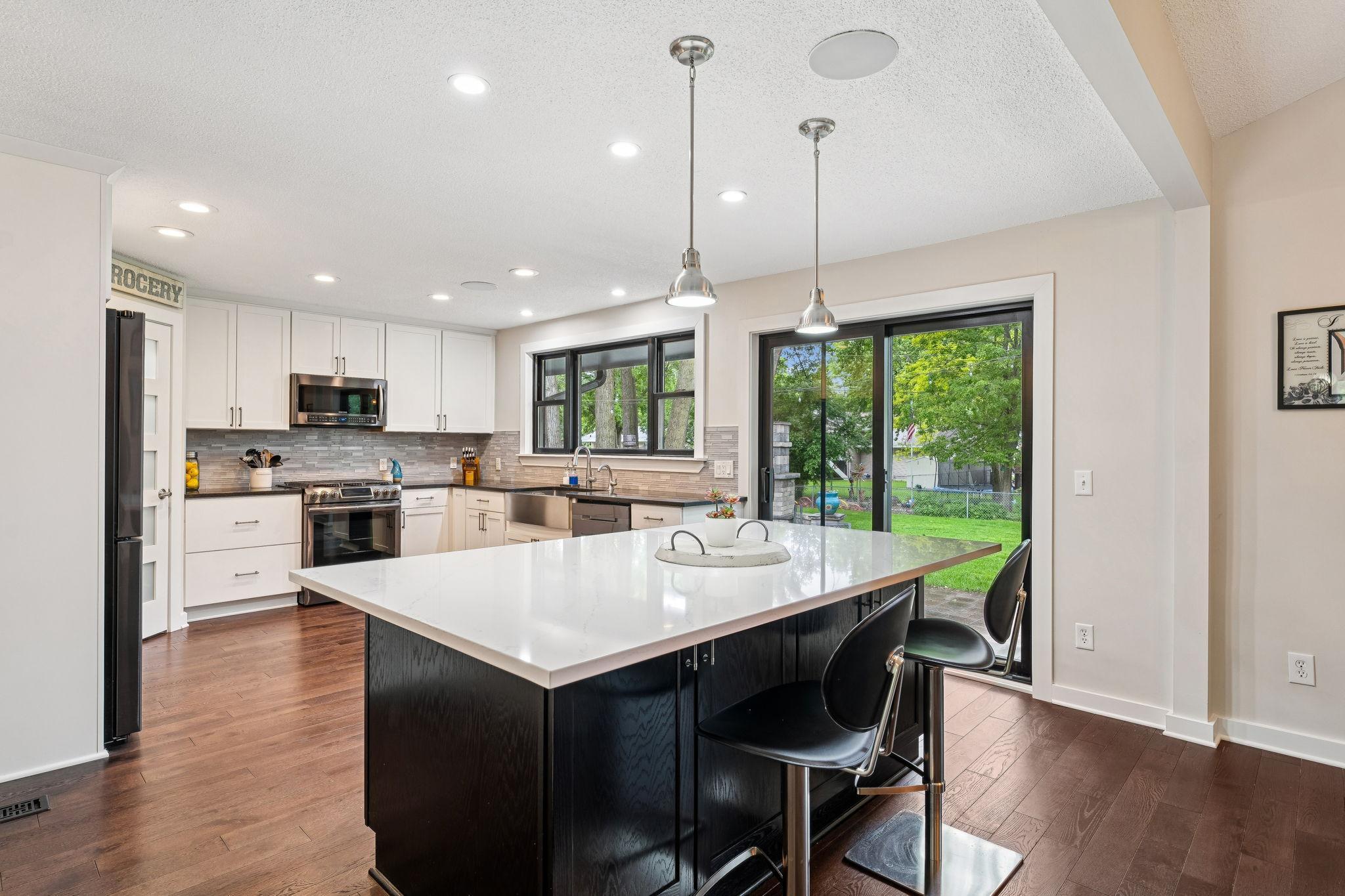 Spacious kitchen features a large quartz island with seating, granite countertops, stainless steel appliances, and a chic tile backsplash. Easy access to the backyard through the sliding doors.