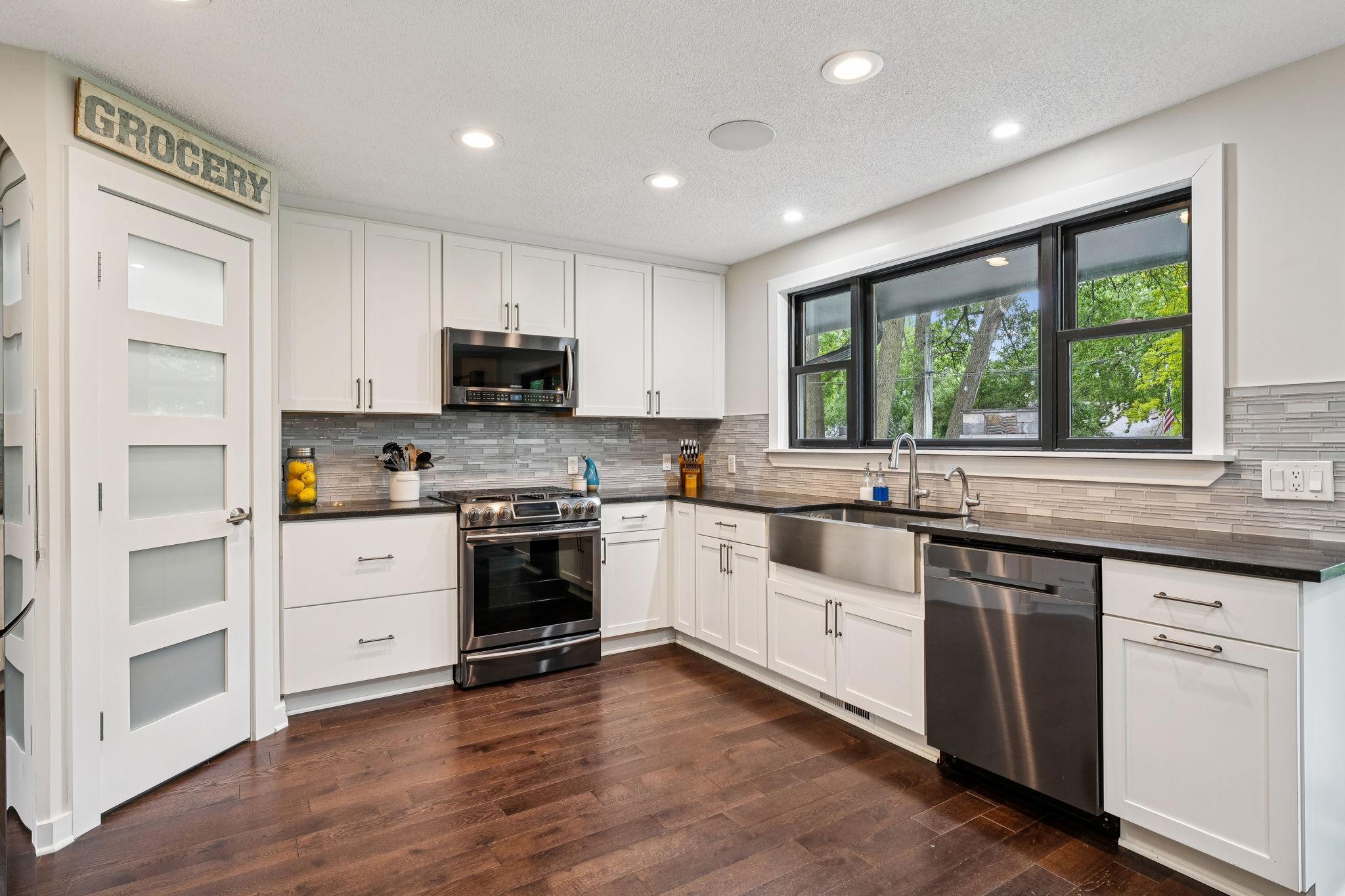 Crisp and modern kitchen with white shaker cabinets, sleek gray tile backsplash, and a stainless steel appliances with a gas range. A walk-in pantry with frosted glass door adds function and style.