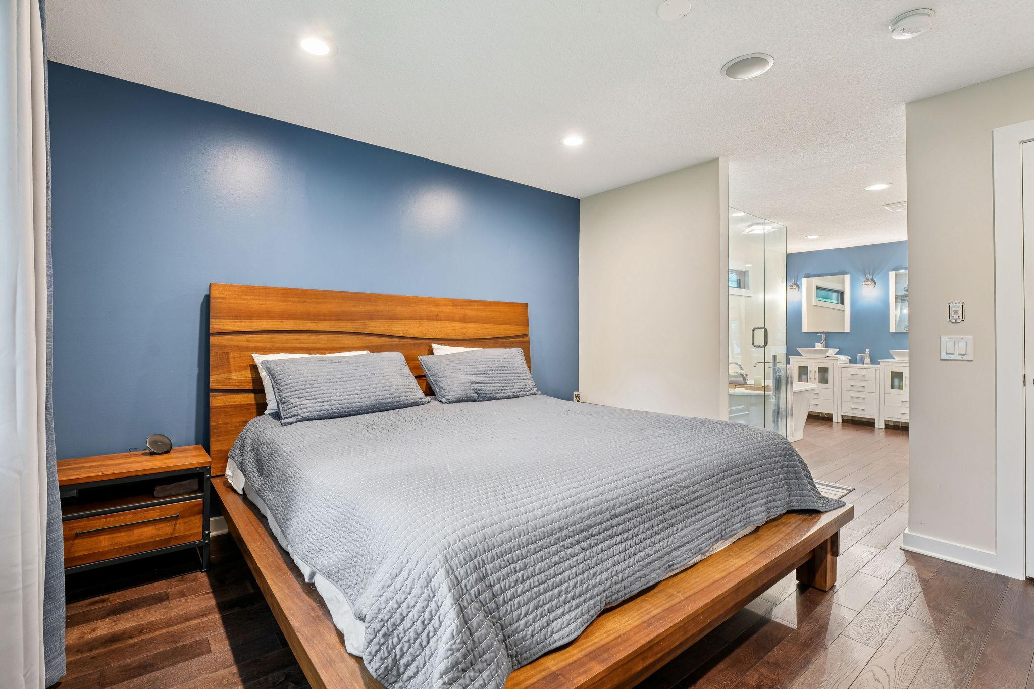 Peaceful primary suite with wood floors, accent wall, and modern recessed lighting.