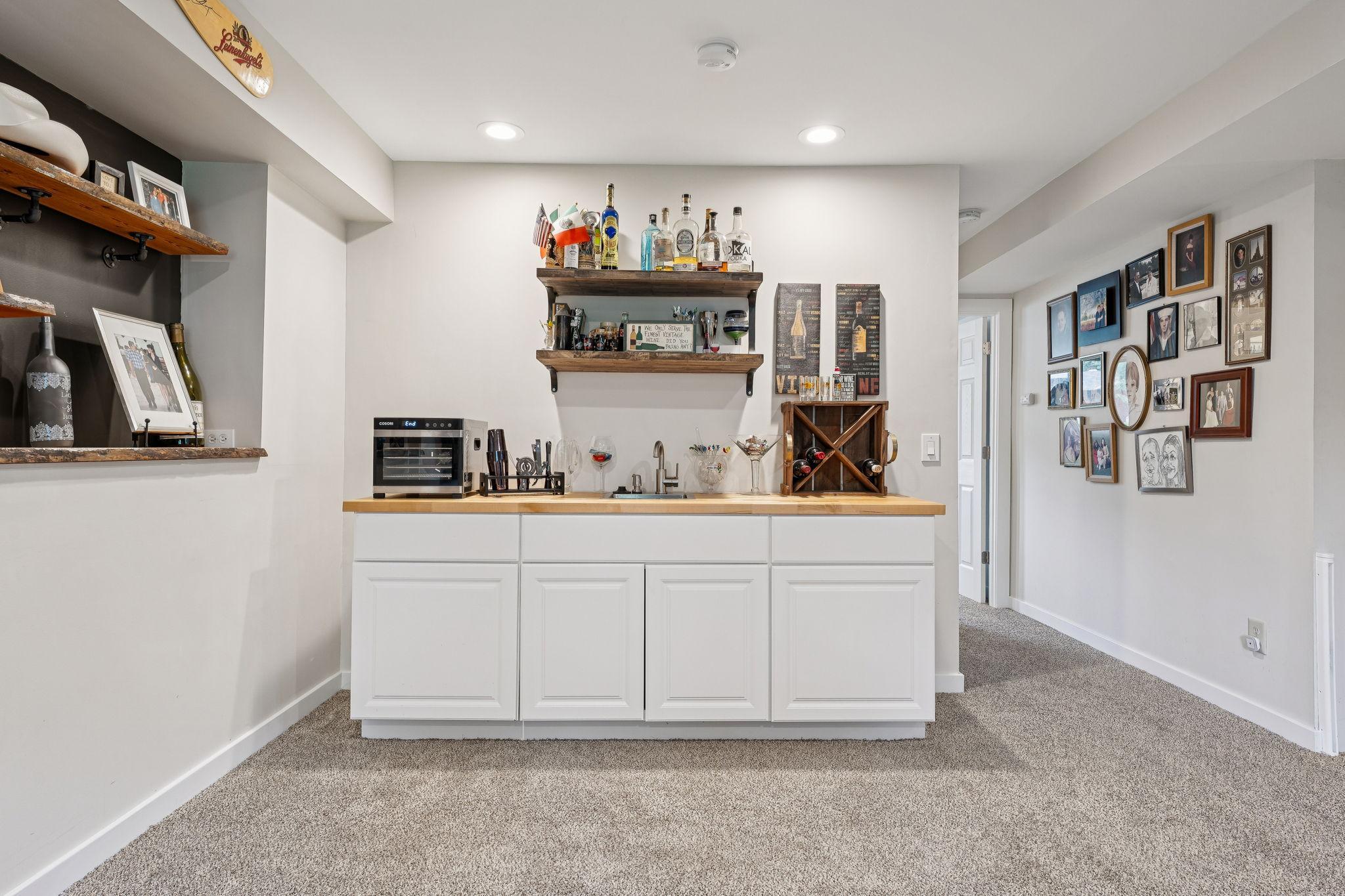 Custom wet bar includes a sink, beverage fridge, butcher block counters, and open shelving for stylish display.