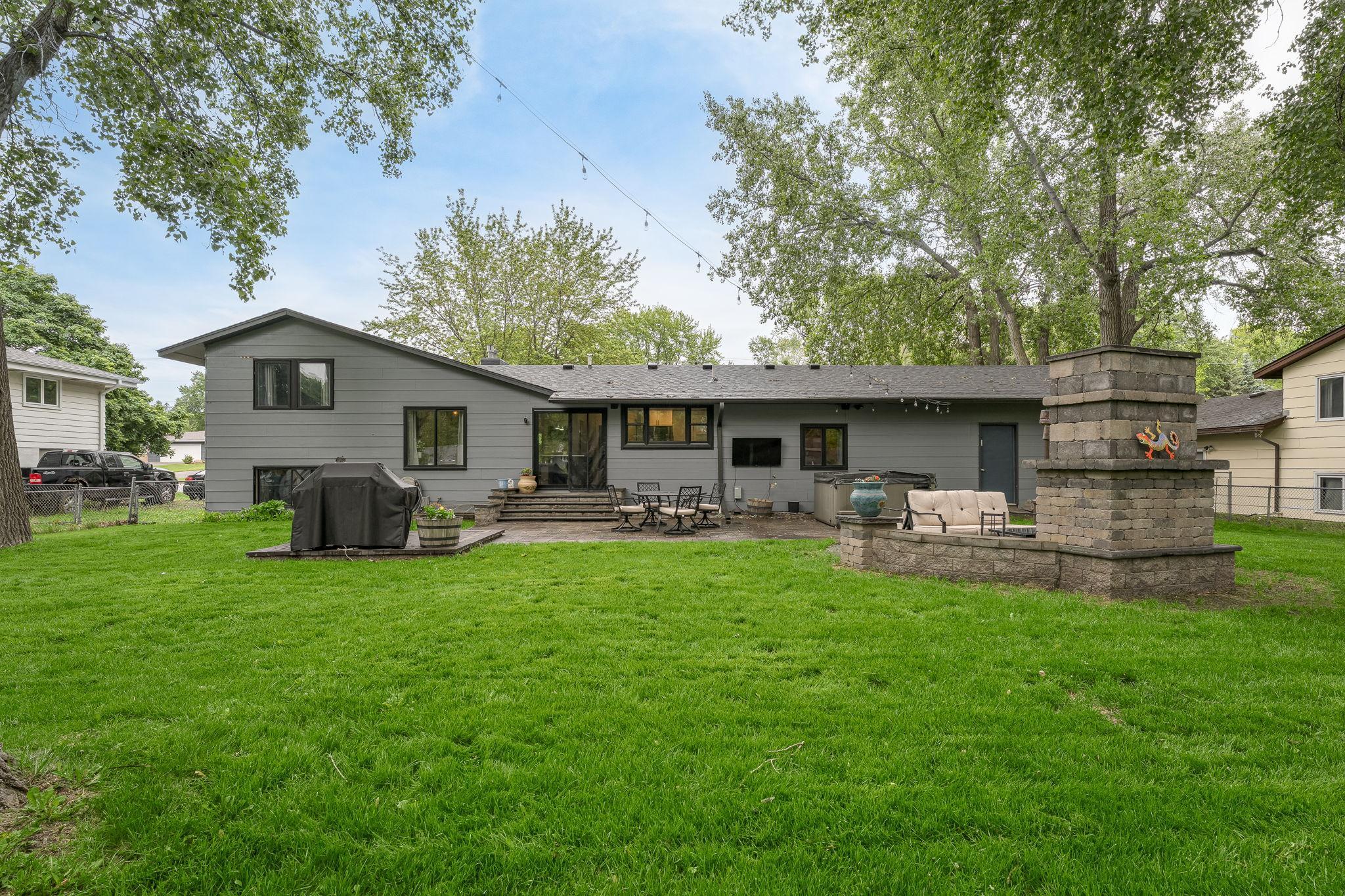 Expansive, fully fenced backyard with lush green lawn, perfect for entertaining or relaxing. Features include multiple patio areas, a built-in stone fireplace, and grilling space.