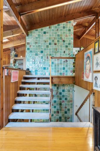 Stunning green tile adds a colorful element to the staircase and fireplace, breaking up the lines of soaring ceilings, skylights, and exposed wood beams with built-in lighting.