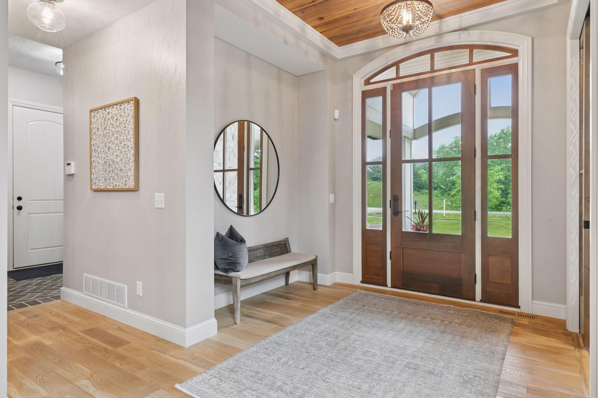 The entryway features a stunning wood-accented ceiling, custom chandelier, and a beautiful glass door with transom windows that fill the space with natural light and charm.