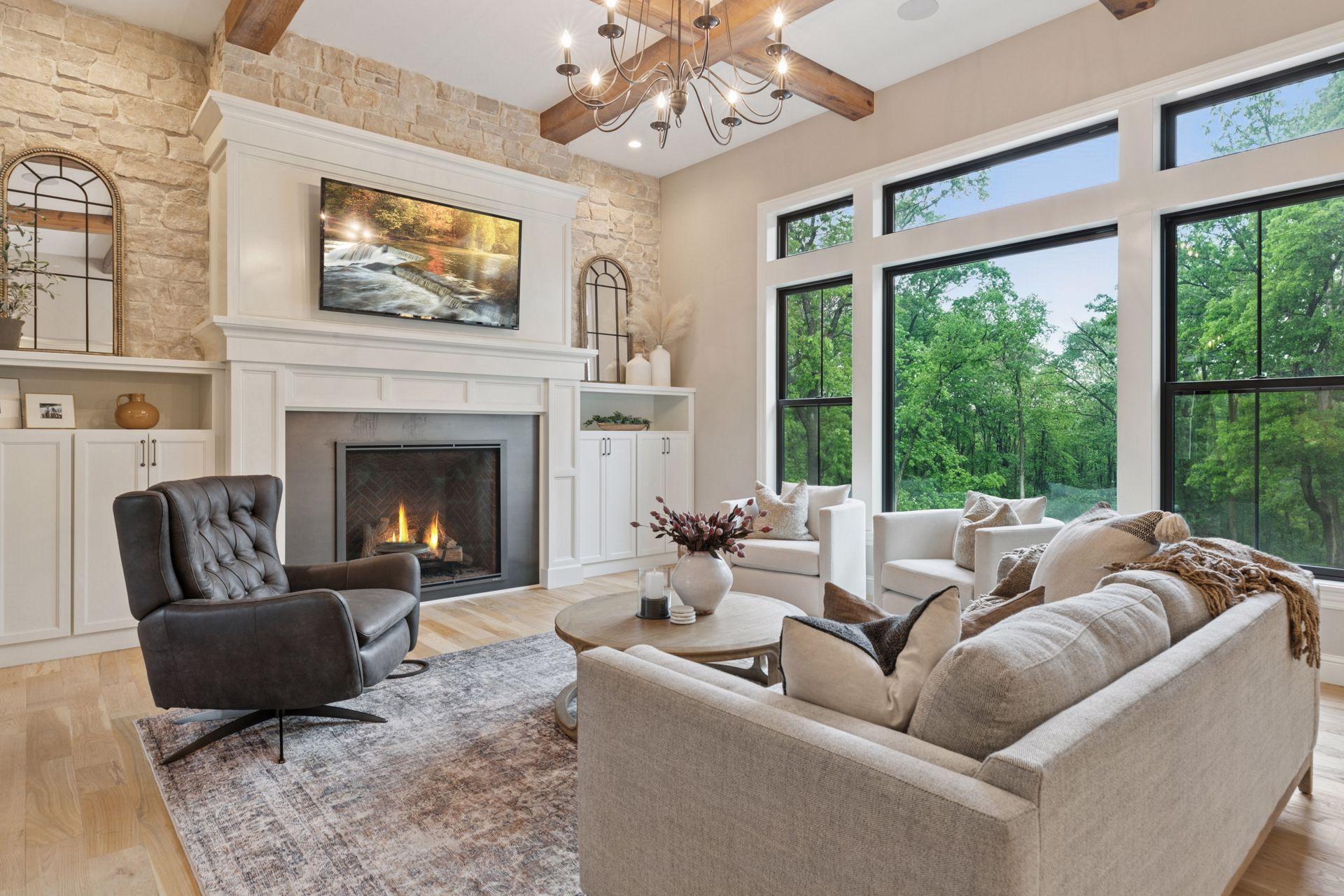 Warm and welcoming great room featuring a stone fireplace, custom built-ins, and expansive windows framing serene wooded views.