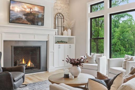 Spacious seating area with cozy textures, fireplace ambiance, and views of backyard pool and the wooded landscape just beyond the windows.