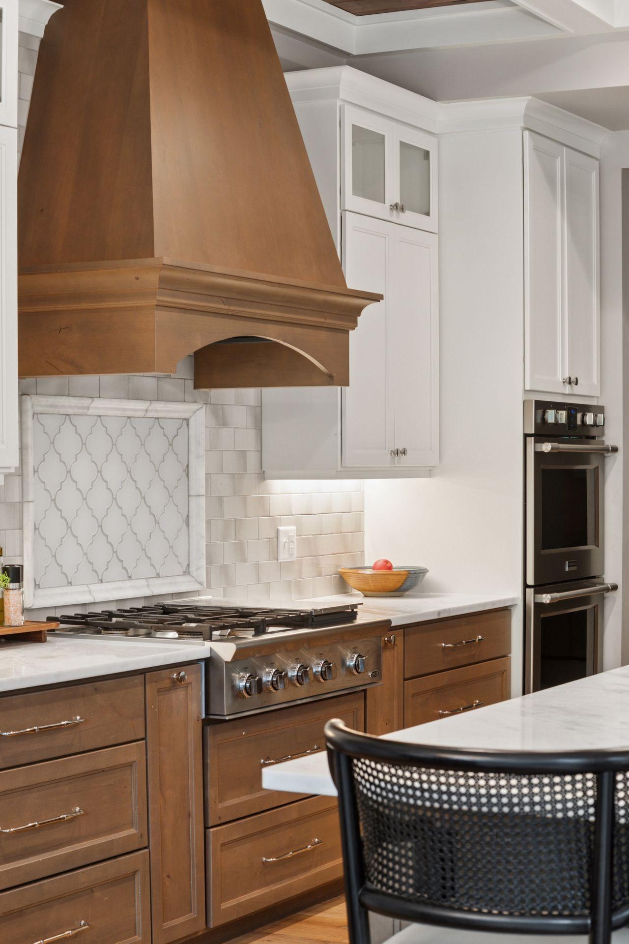 Close-up of the gourmet range area featuring a custom wood hood, designer tile backsplash, and elegant white cabinetry with soft-close drawers.