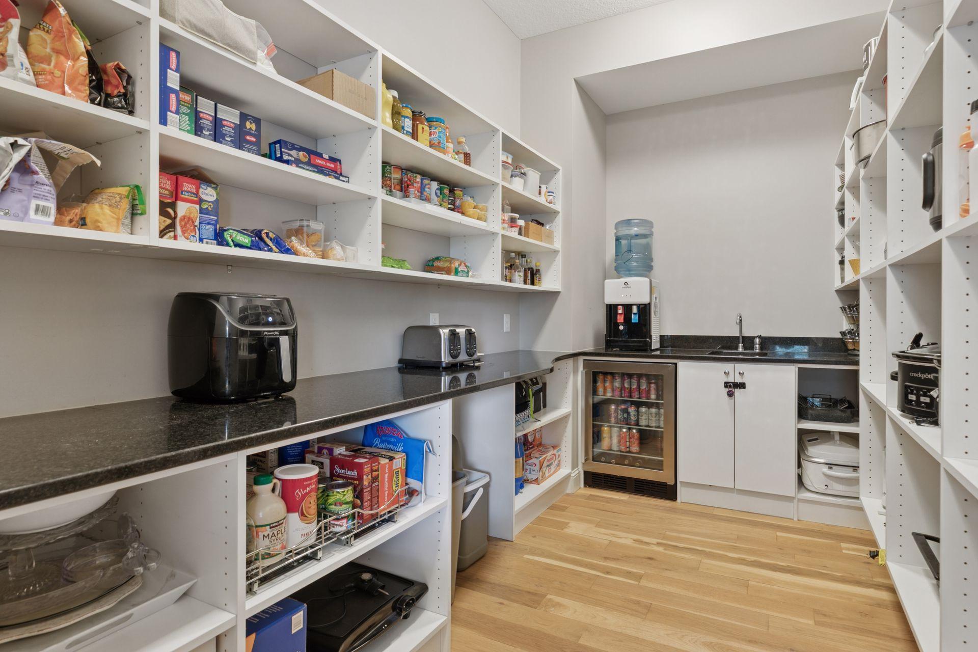 Spacious walk-in pantry with abundant custom shelving, beverage fridge, prep sink, and generous counter space—perfect for storage and entertaining prep.
