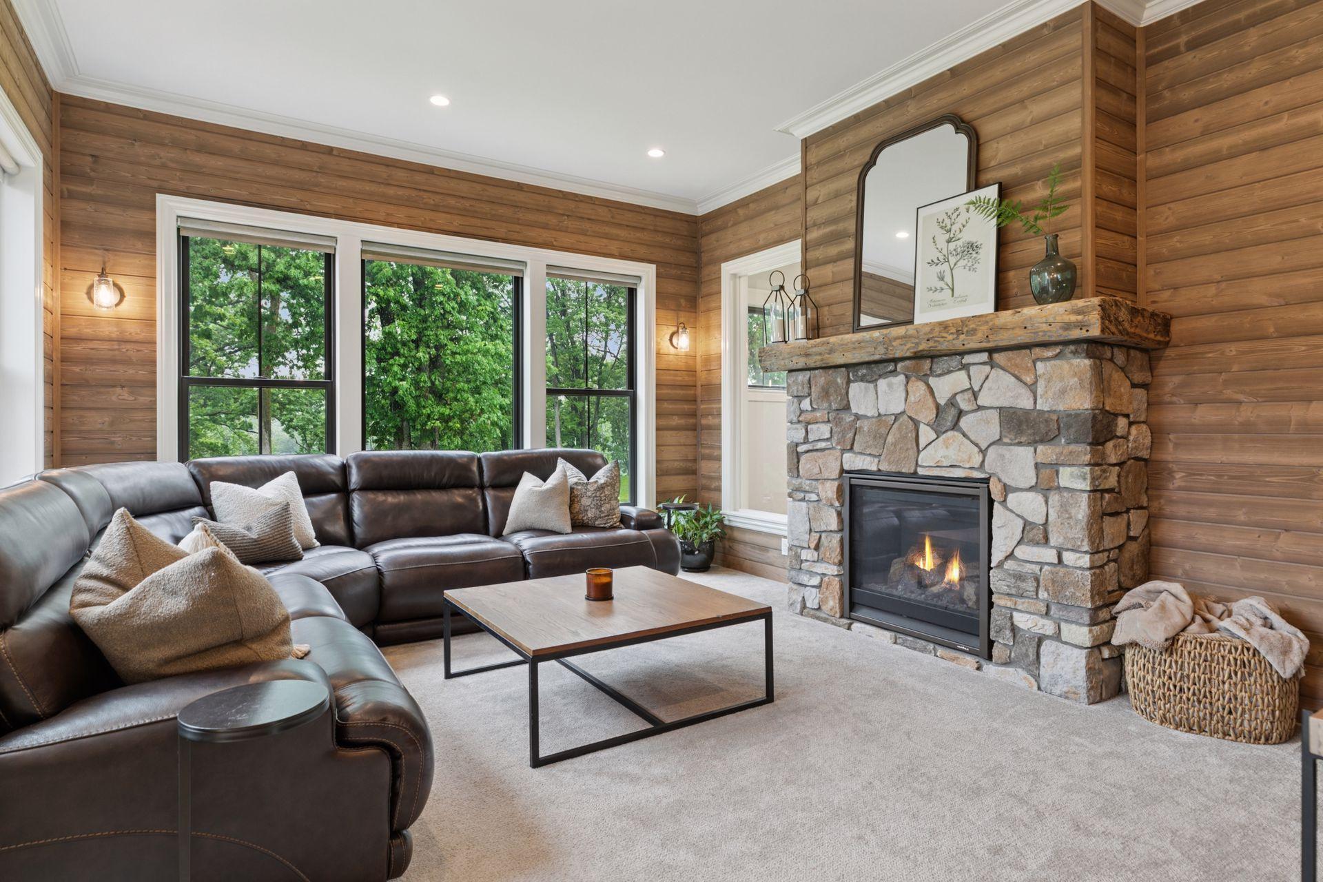 Inviting sunroom with stone-surround gas fireplace, warm wood-paneled walls, and panoramic views of lush greenery and the indoor sport court. A comfortable retreat for reading or casual gatherings.