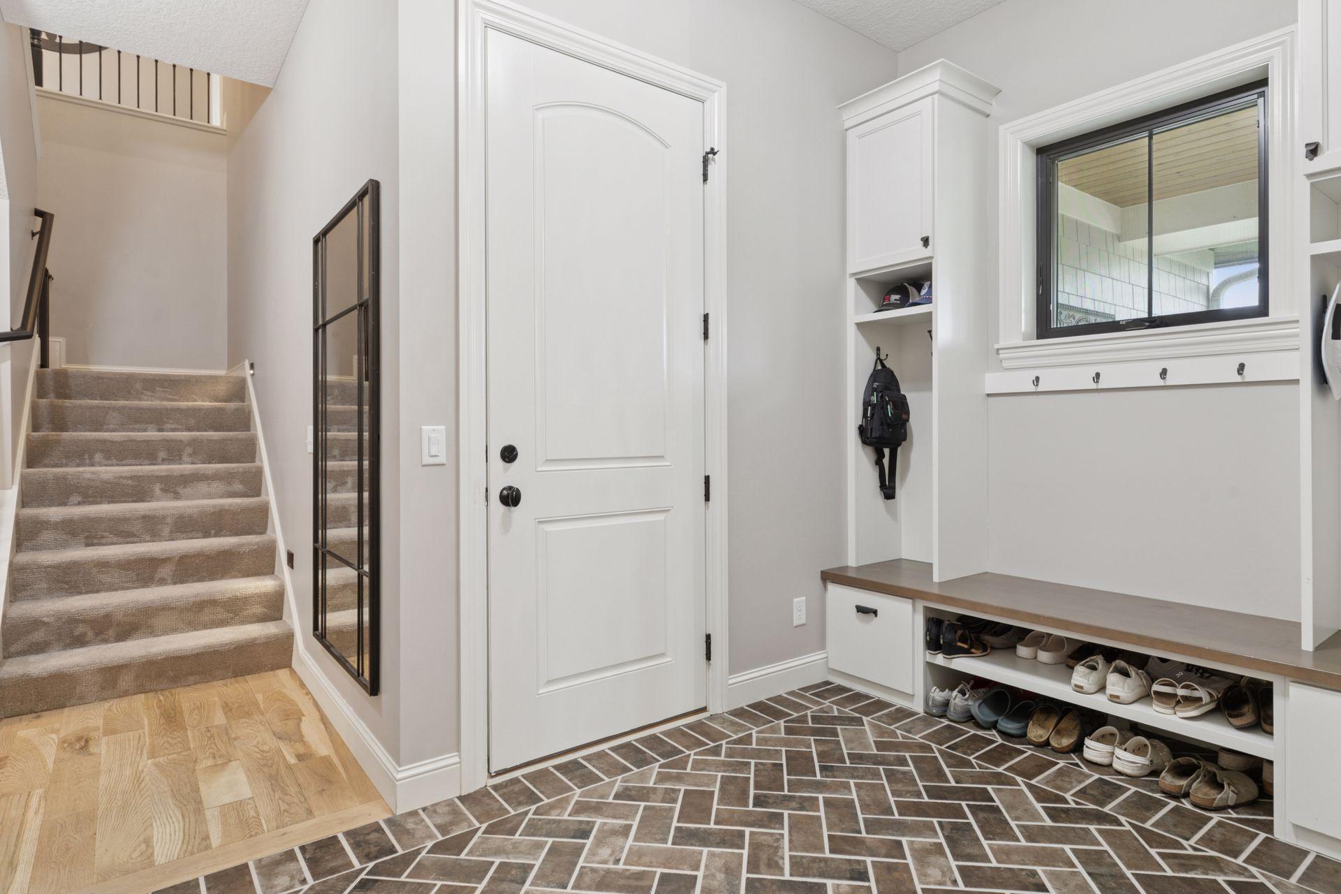Stylish and functional mudroom with built-in cubbies, bench seating, and ample shoe storage. A herringbone tile floor adds visual interest and durability, with direct access to the garage and carpeted stairway to upper levels.