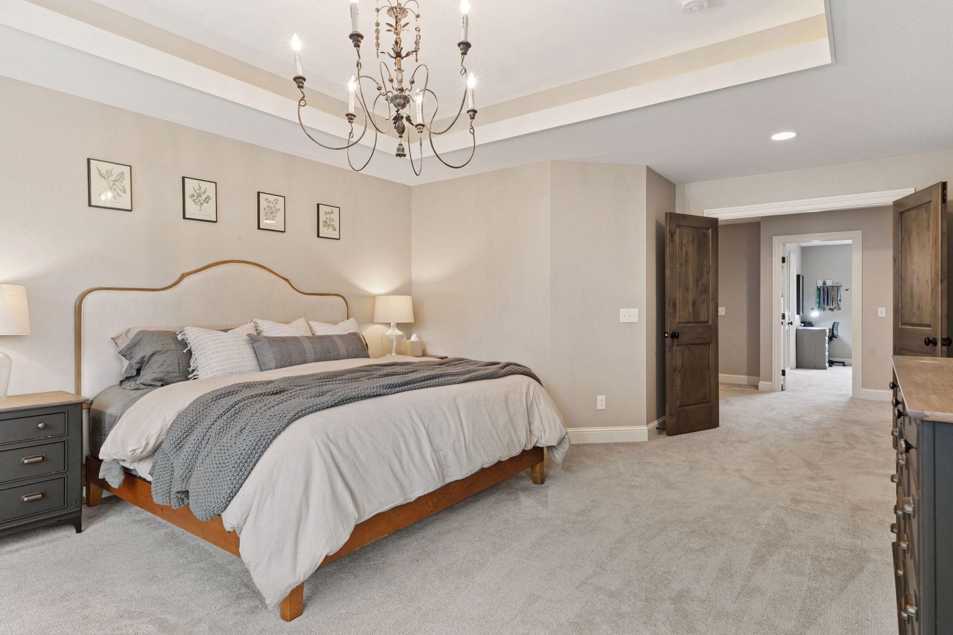 A view of the owner’s suite showcases soft neutral tones, a stylish chandelier, and double-door access to the hallway and adjoining spaces.