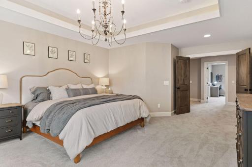 A view of the ownerâs suite showcases soft neutral tones, a stylish chandelier, and double-door access to the hallway and adjoining spaces.