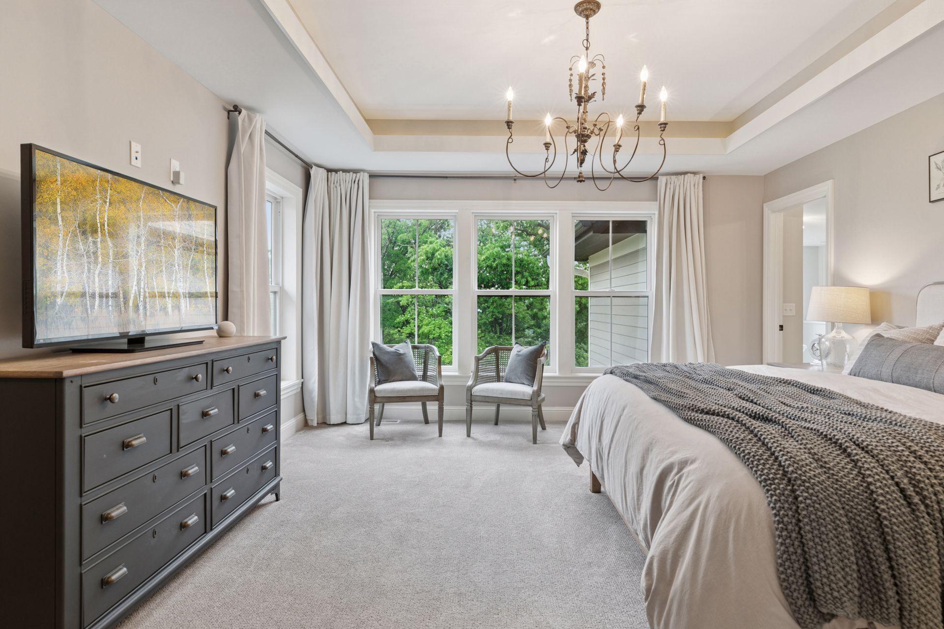 Natural light floods the bedroom through expansive windows, highlighting a peaceful seating nook perfect for reading or relaxing.