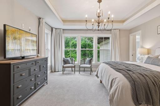 Natural light floods the bedroom through expansive windows, highlighting a peaceful seating nook perfect for reading or relaxing.