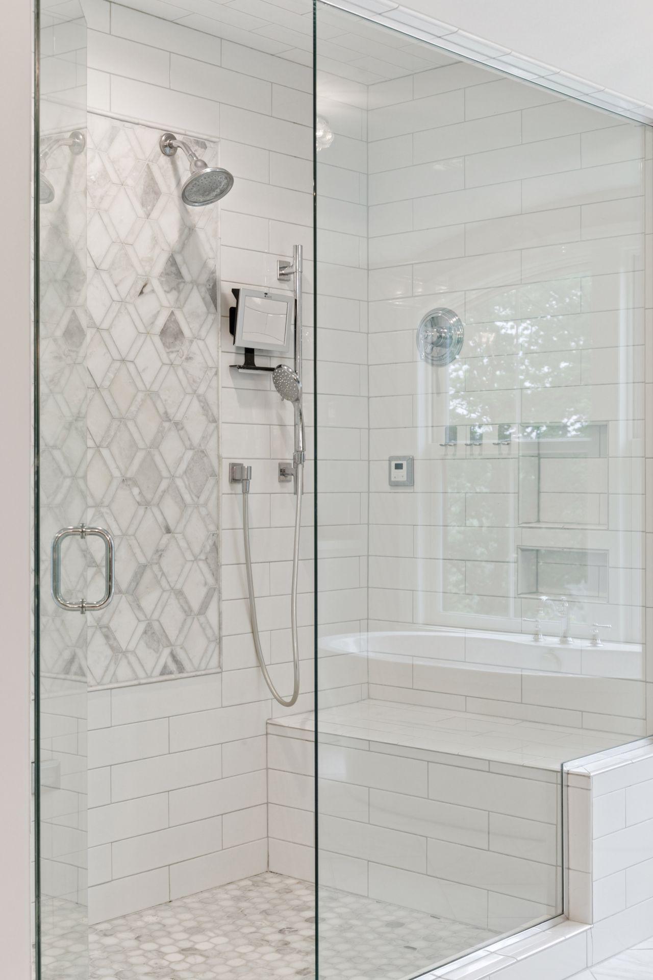 The large walk-in shower features clean and bright finishes, including a custom tile inlay, and a large bench.